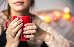 Photo of a woman holding a coffee mug, with festive nail polish from a nail salon running a holiday promotion.